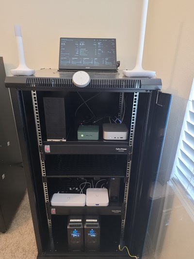 Full view of the server rack with a laptop and wireless access points on top, computers on shelves, and two UPS units below.